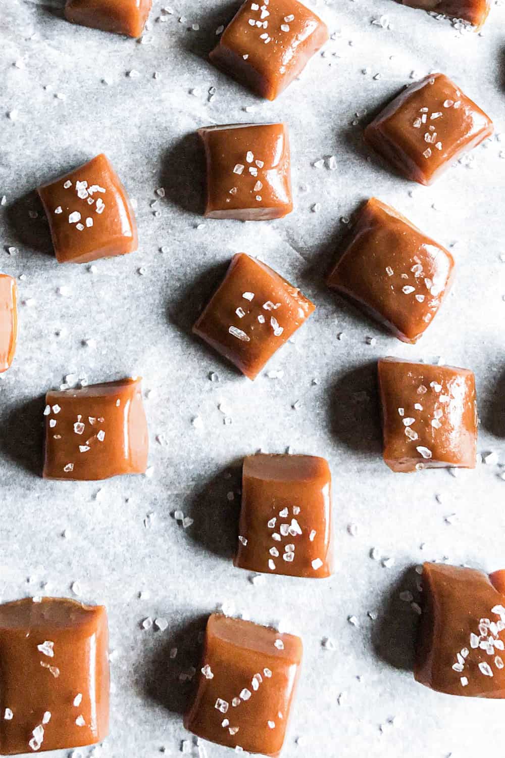 whiskey salted caramels on parchment paper sprinkled with sea salt.