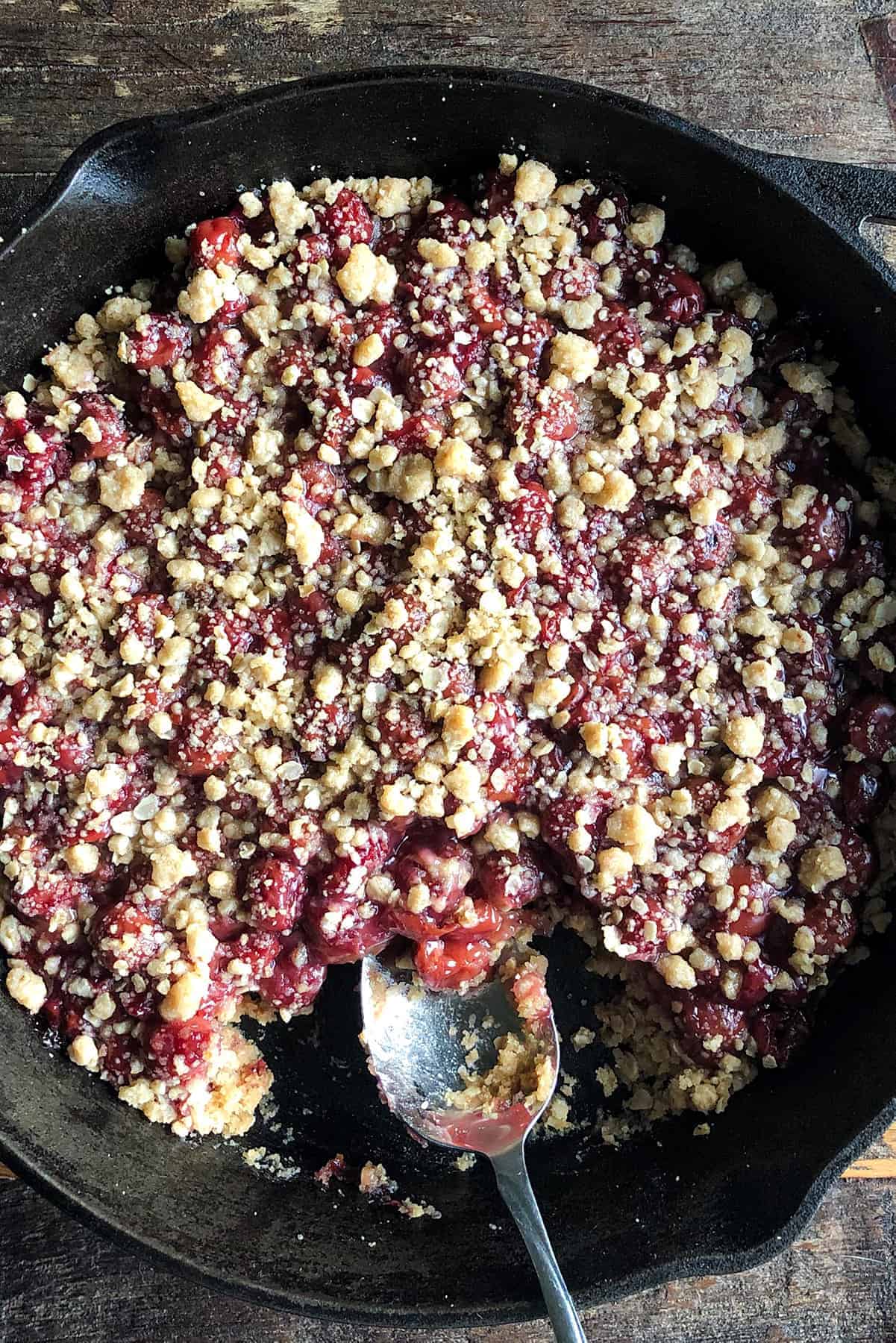 Grandma's sour cherry crisp in a cast-iron pan with a piece out of it.