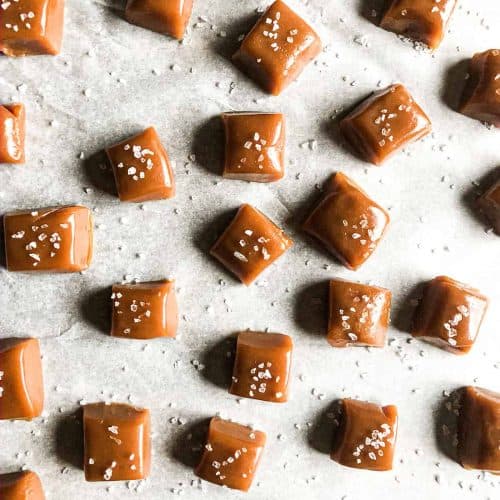 Whiskey salted caramels on parchment paper, sprinkled with sea salt.