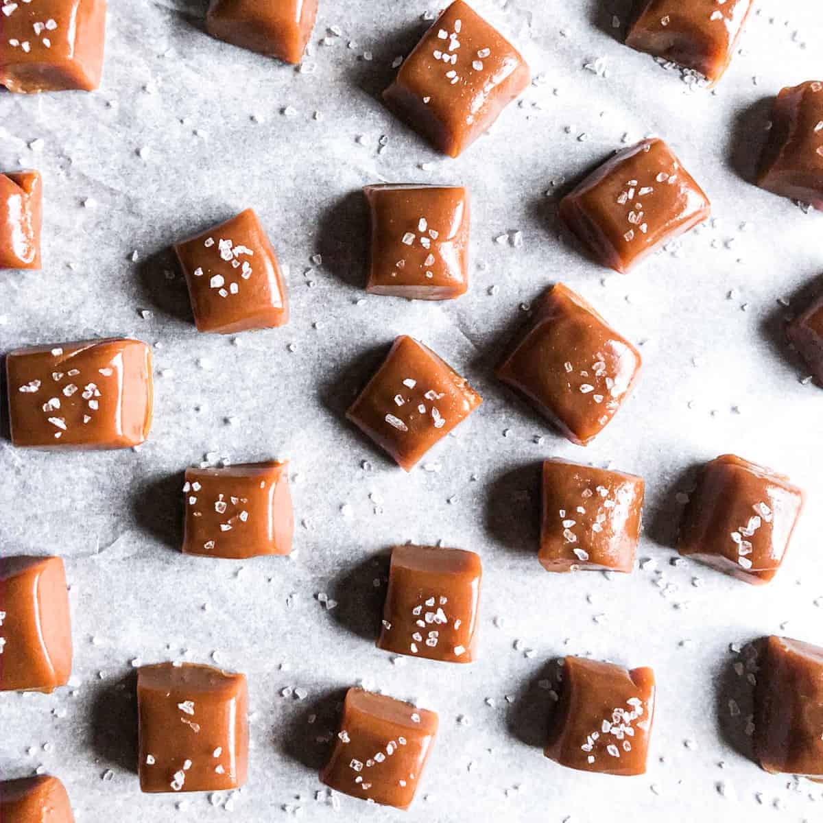 Whiskey salted caramels on parchment paper sprinkled with sea salt.